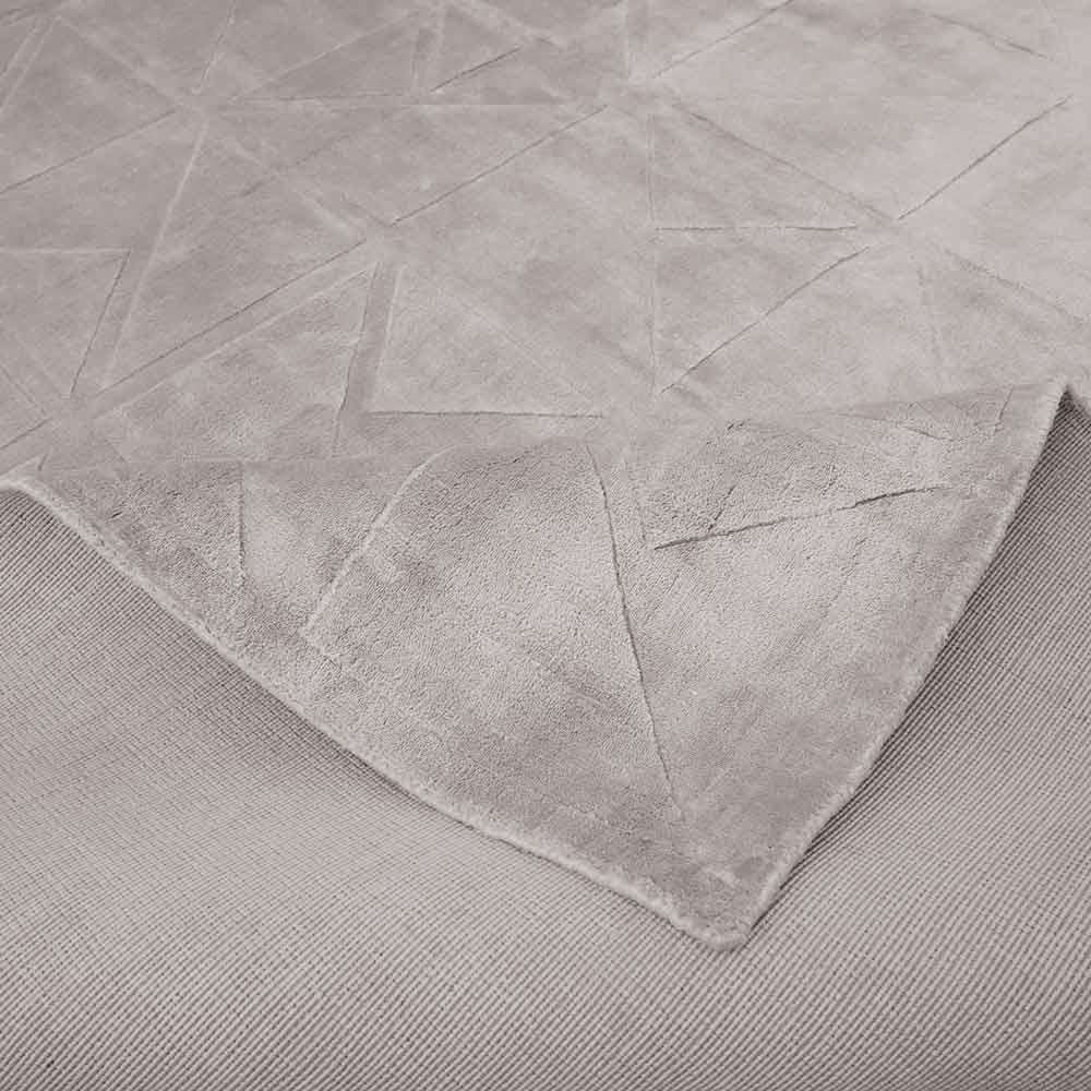 Detailaufnahme eines strukturierten Teppichs mit geometrischem Muster in neutralen Farben wie Grau oder Beige, teilweise umgeschlagen, um die Unterseite zu zeigen.