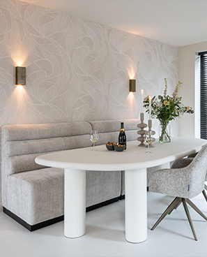 Eleganter Essbereich mit weißem Tisch, grauer Bank, goldene Wandleuchten und Tischdeko mit Champagner und weißen Blumen