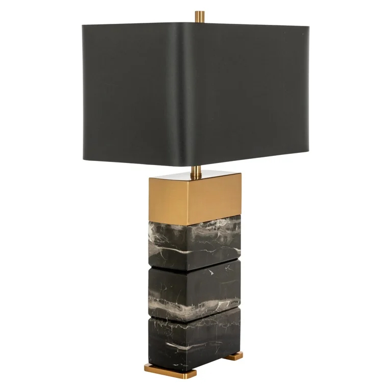 Moderne Tischlampe mit einem Sockel aus gestapelten Steinen in Schwarz- und Grautönen, verziert mit goldfarbenen Metalldetails und einem rechteckigen, dunklen Lampenschirm.